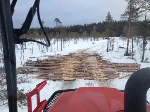 Utsikt från hytten över ett timmerupplag på en snötäckt avverkningsplats.